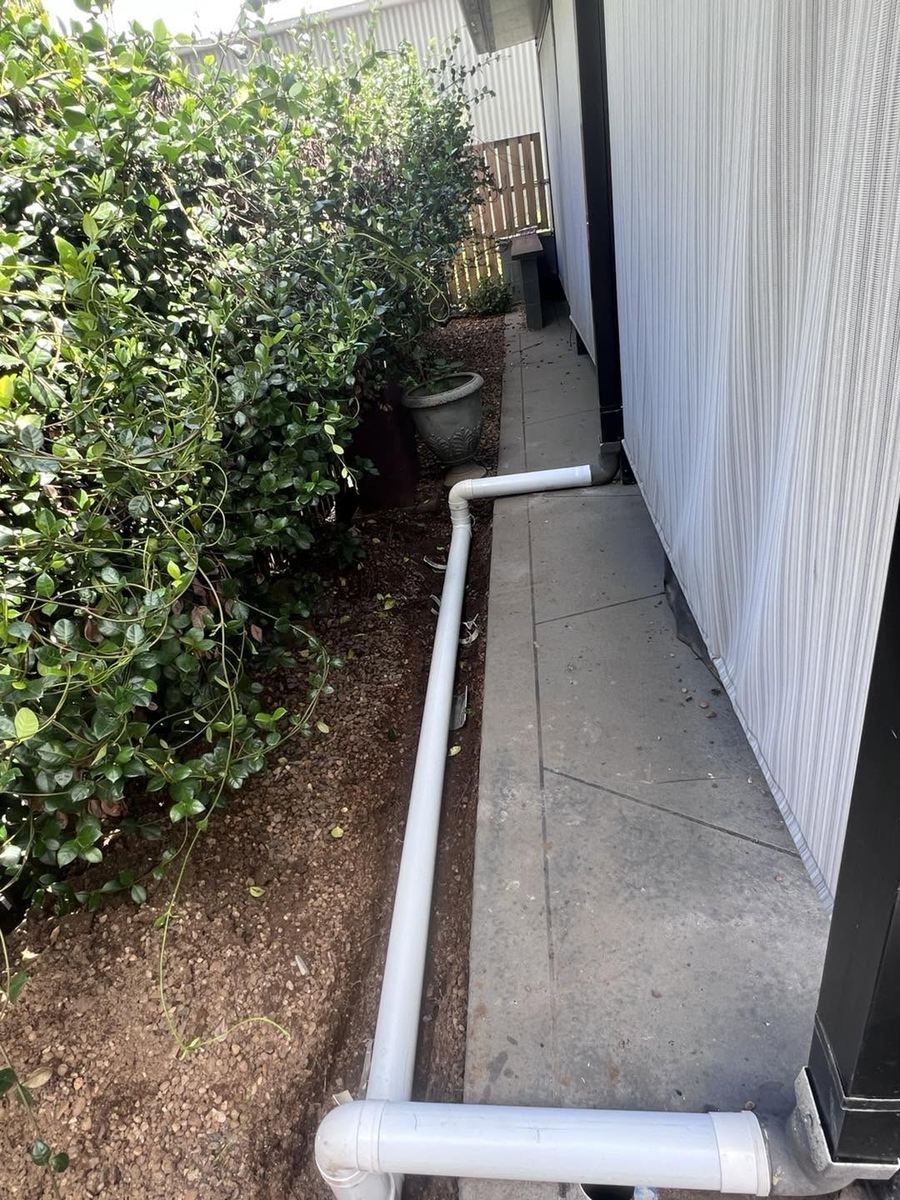New white PVC stormwater pipe run clipped along the side of a house next to a garden bed