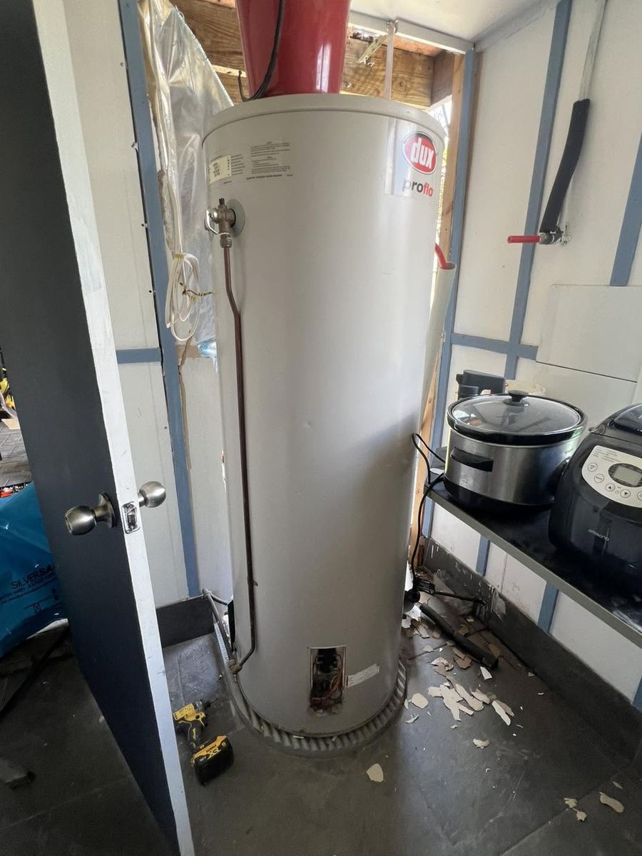 Old Dux Proflo hot water unit being removed from a narrow internal laundry cupboard