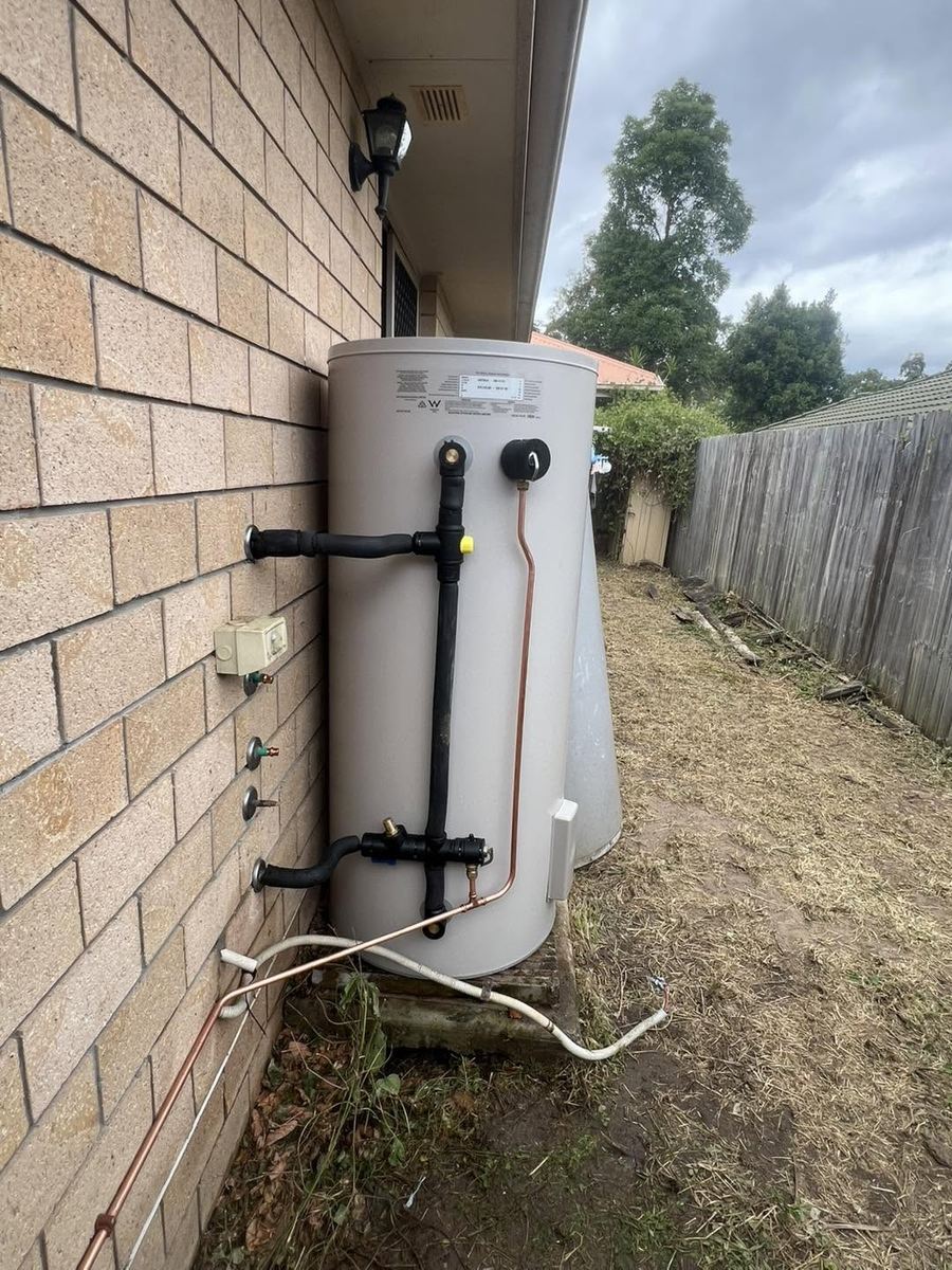 New storage hot water system installed against a brick wall with lagged pipework and copper relief line