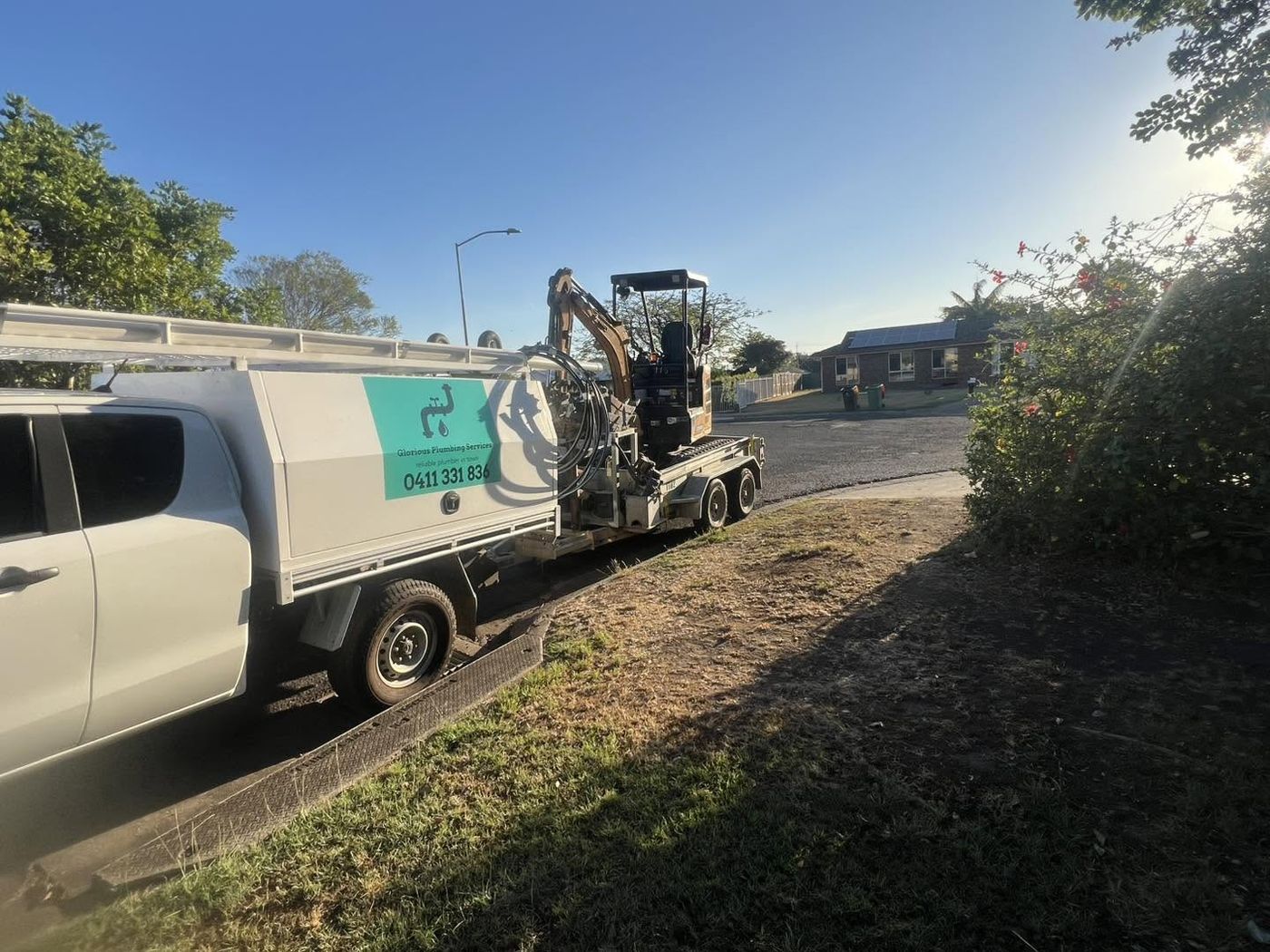 Glorious Plumbing Services ute towing a trailer with a mini excavator loaded, parked on a suburban street